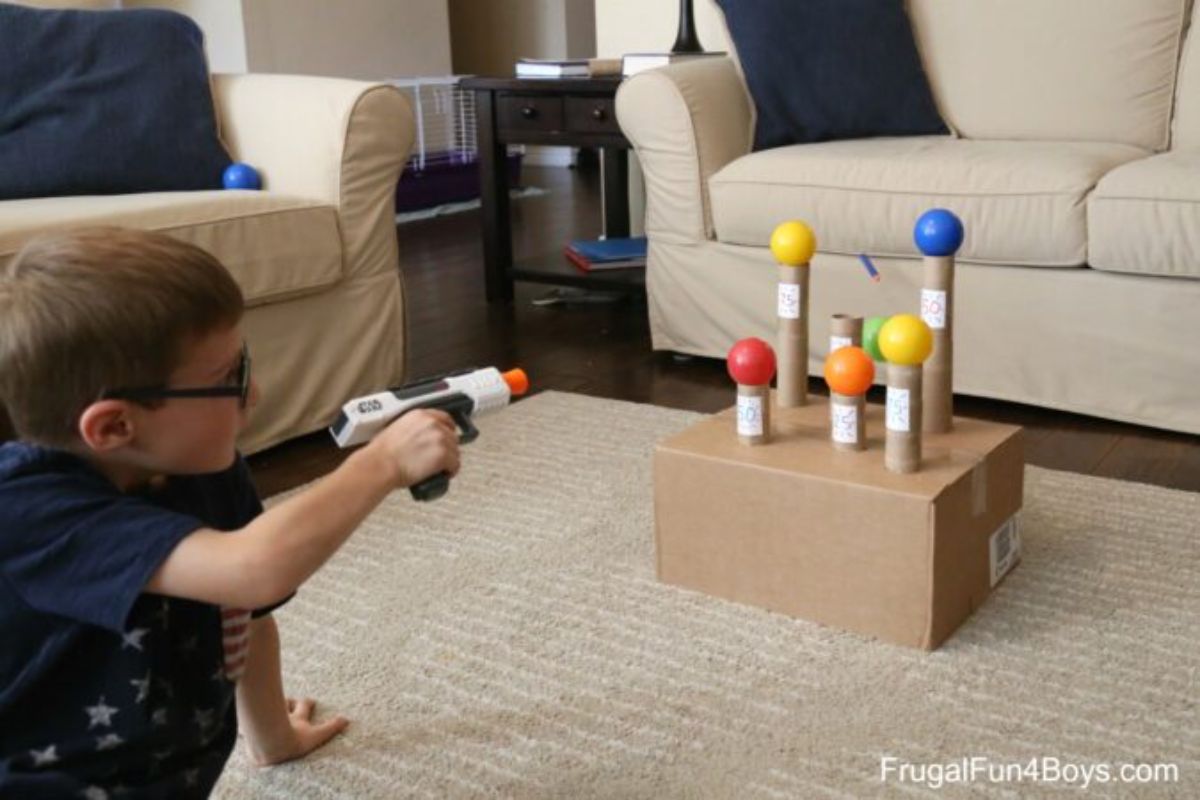 a boy aims a nerf gun at some balls balanced on toilet rolls