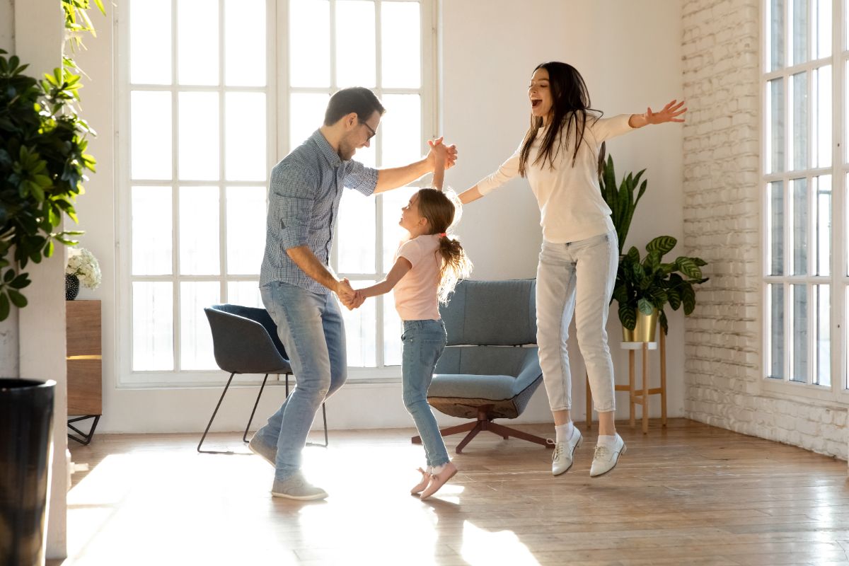 a man, a woman and a young girl dance in a birght and airy room