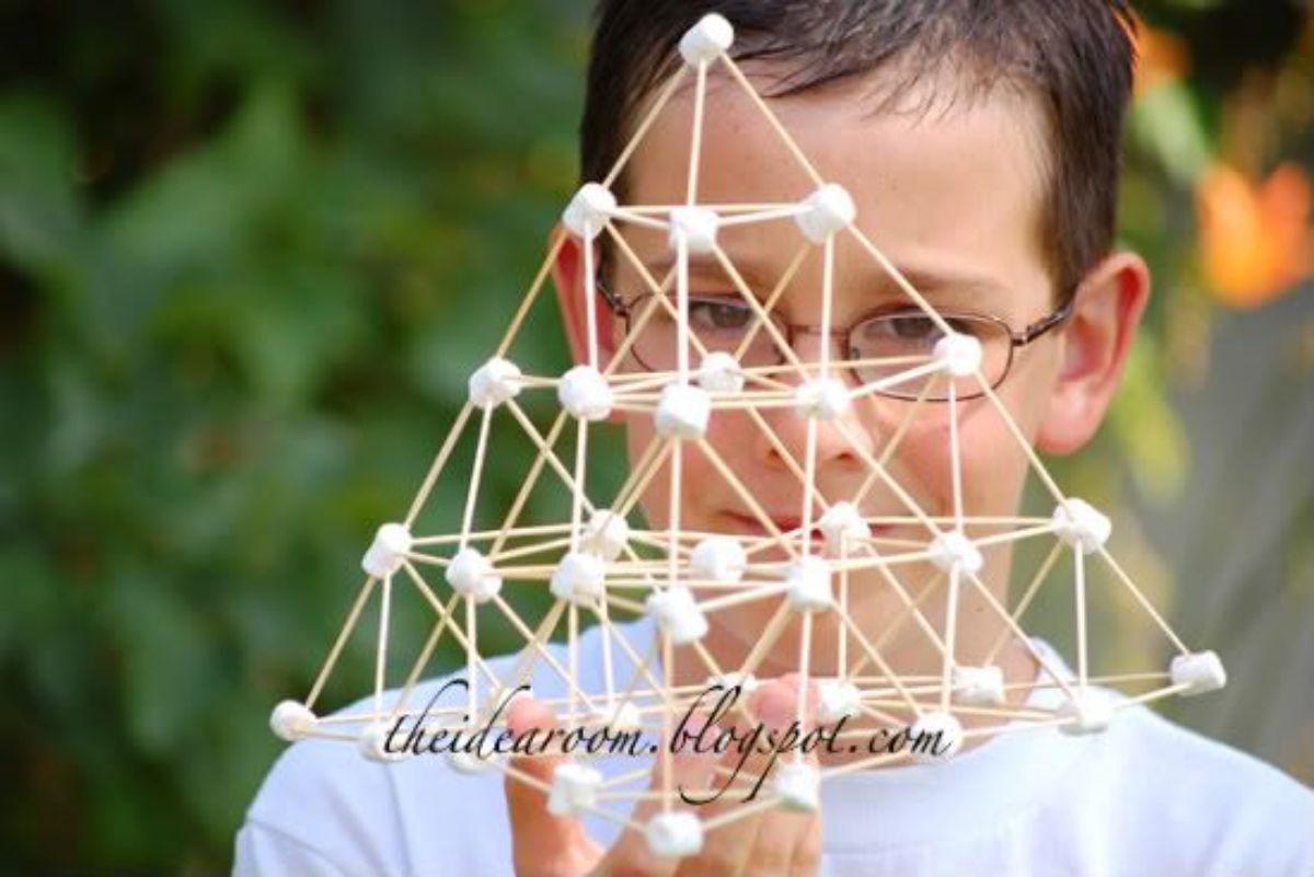 a boy holds a pyramid made from toothpicks and marshmallows