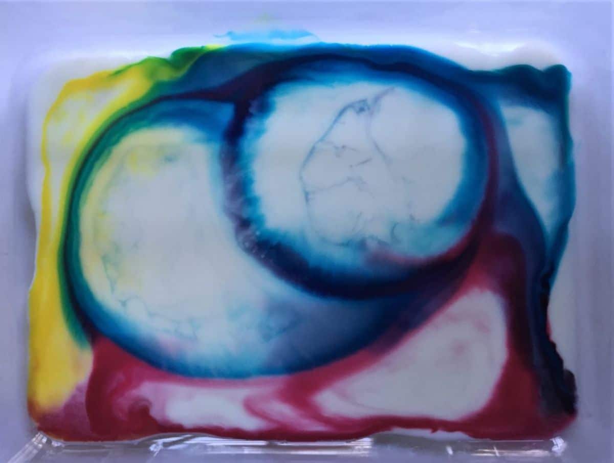 in a plastic tray is a white liquid with blue, yellow and red marbled inks in it