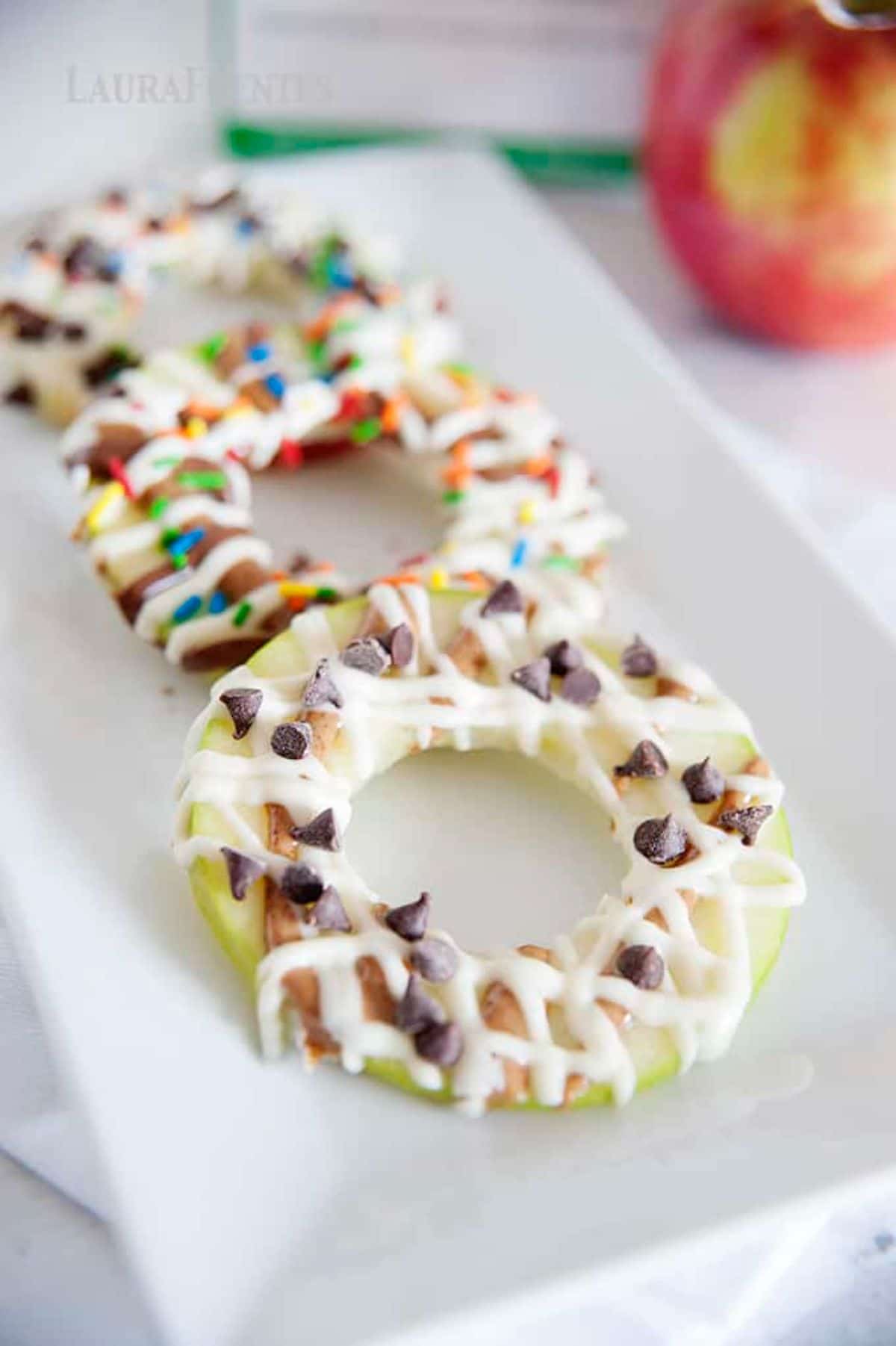 on a rectangular plate are 3 apple slices drizzled with chocolate and sprinkles