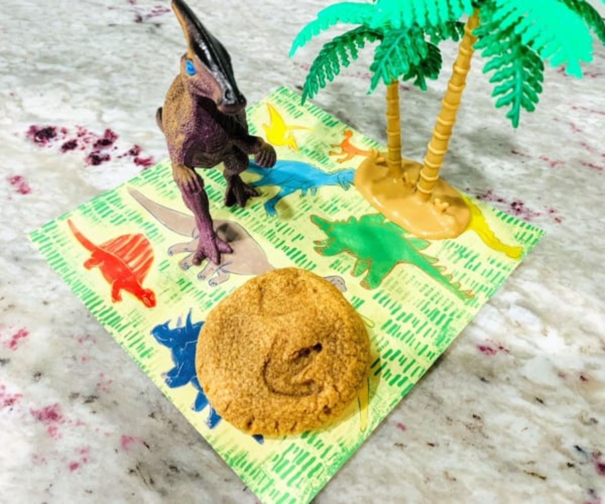 on a dinosaur napkin is a plastic palm tree, a plastic dinosaur and a cookie