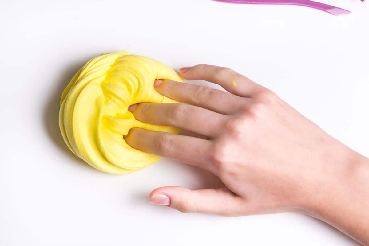 a hand pushes into a pile of yellow playdough