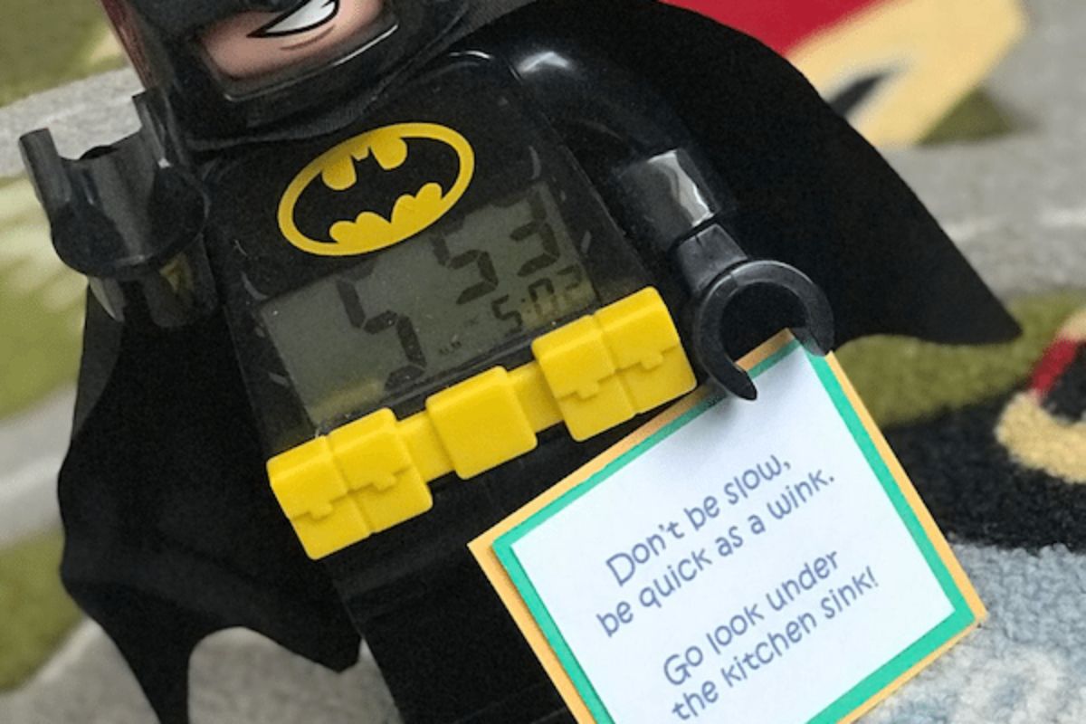 A lego batman is holding a square piece of card that says "Dont be slow be quick as a wink. Go look under the kitchen sink"