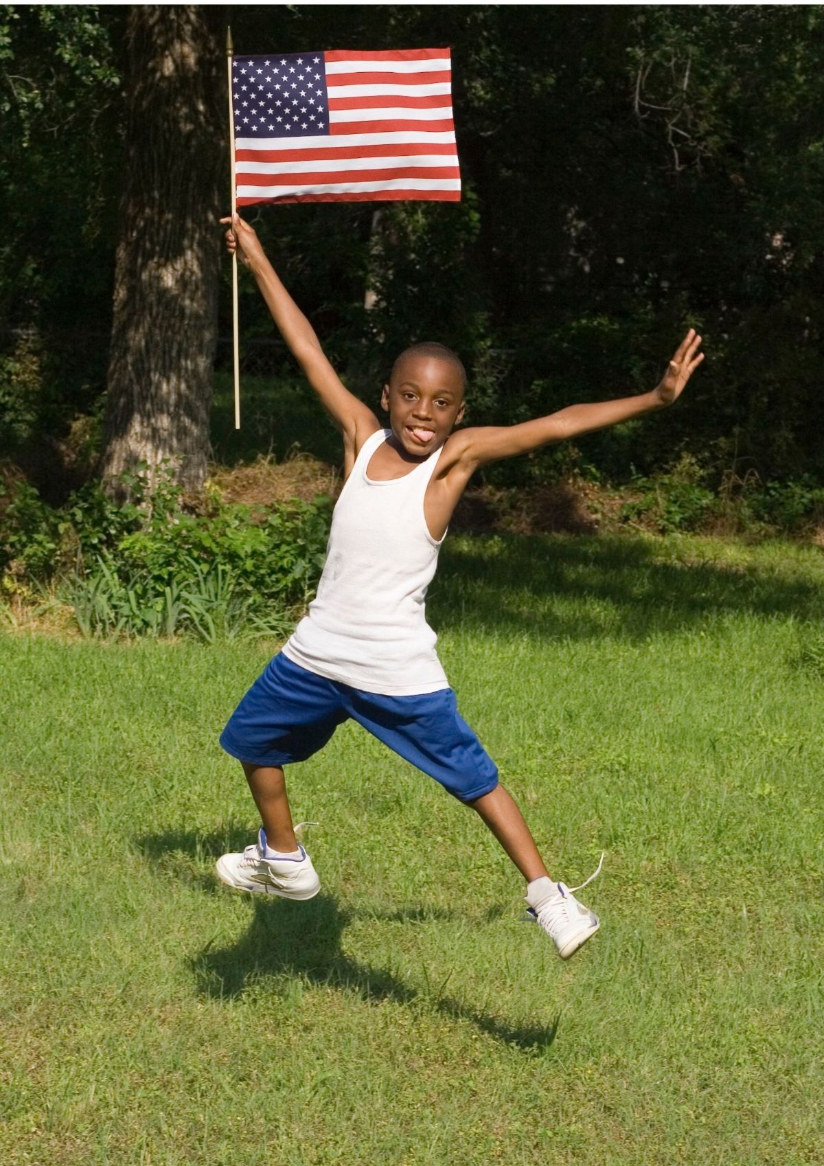 a boy holds an american flag in a field, while jumping in the air
