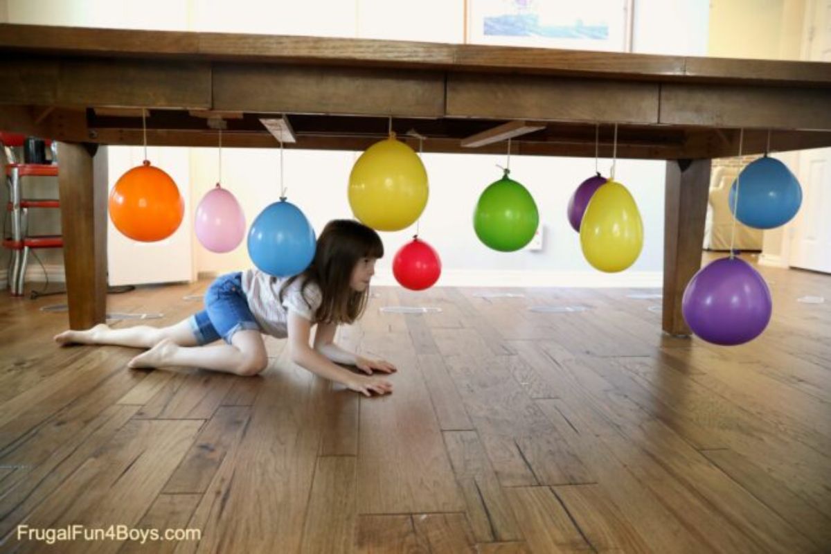 a girl crawls under a table which has balloons dangling from its underside