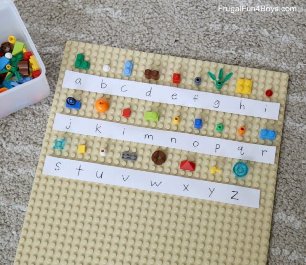 a sand colored lego board has strips of paper with the alphabet written on them. A lego brick is assigned to each letter