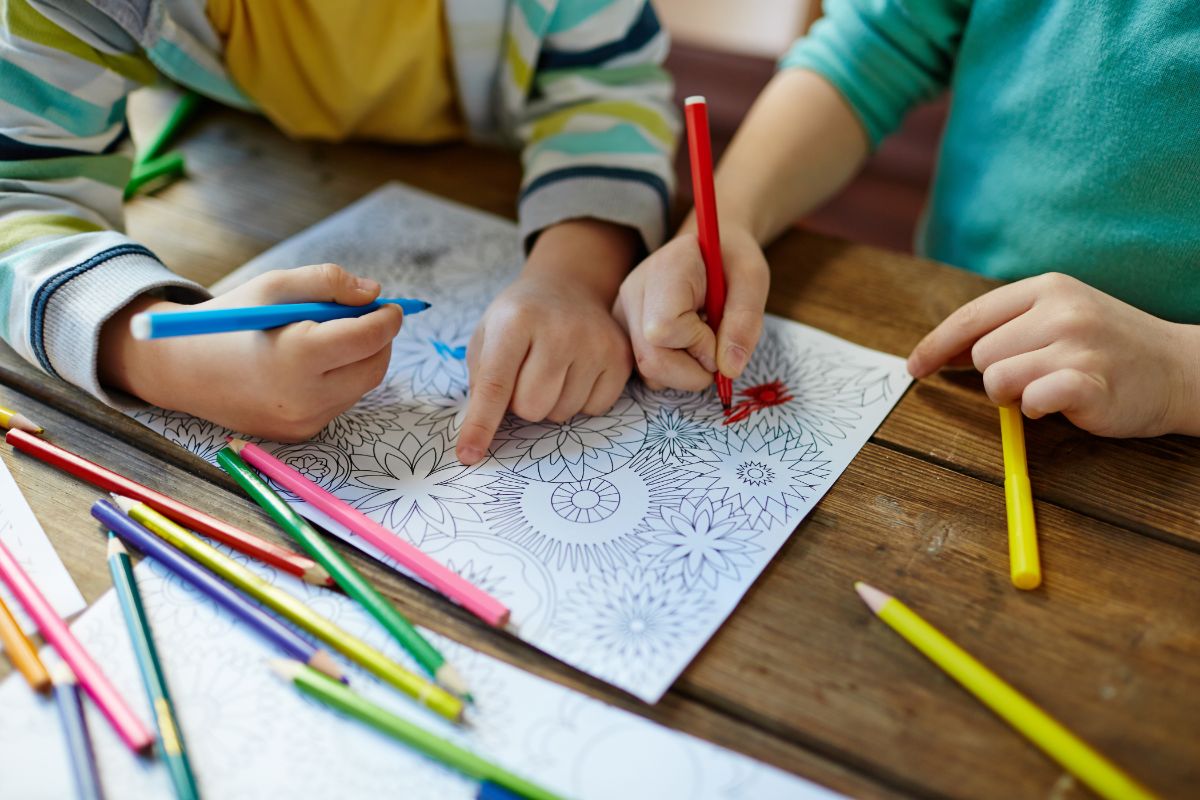 2 children coloring in a geometric pattern with colored pencils scattered around