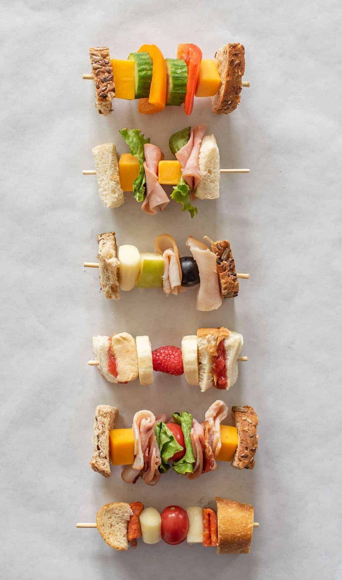 6 skewers are filled with diffferent sandwich combinations