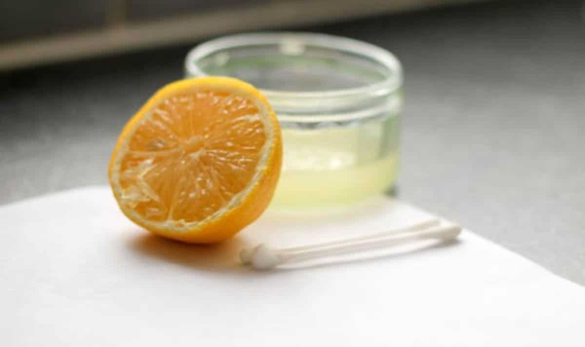 a glass jar of lemon water on a table with 2 cotton buds and half a lemon in front of it