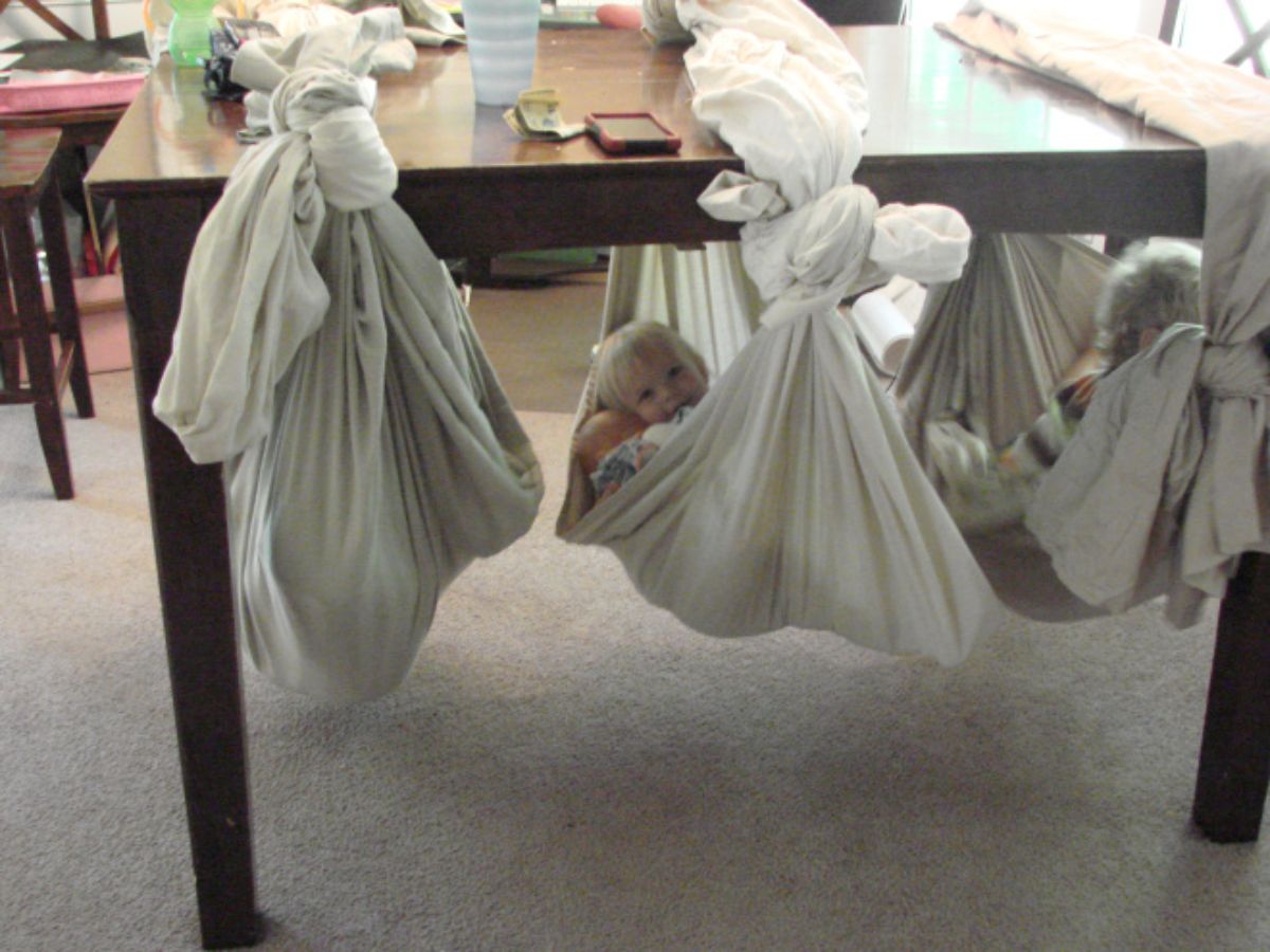 a child hangs from a hammock made from a sheet tied around the table