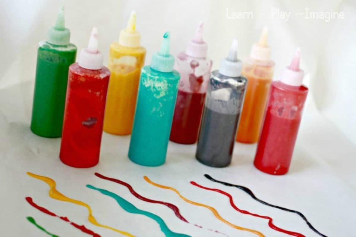 on a white background are 9 bottles of paint in various colors. There are lines of paint squeezed out in front of the bottles