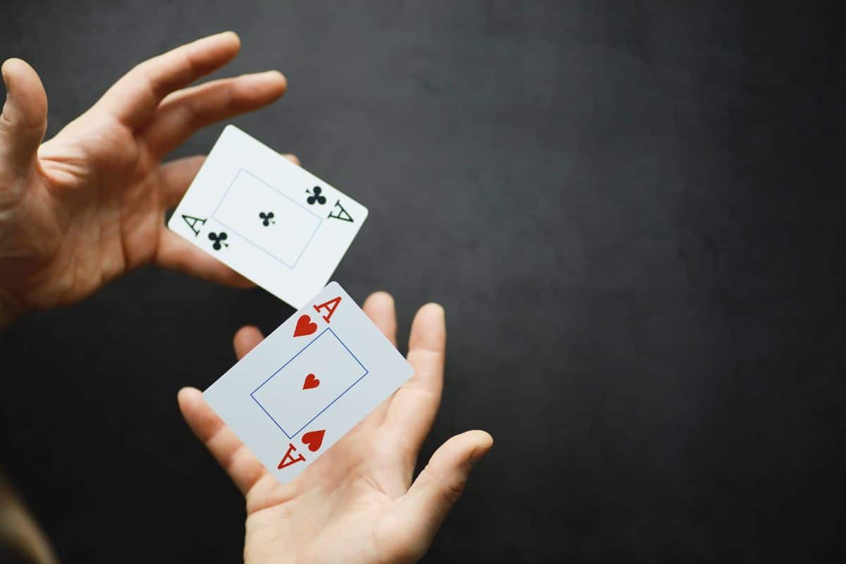 two hands hold an ace of clubs and an ace of hearts in front of a black background