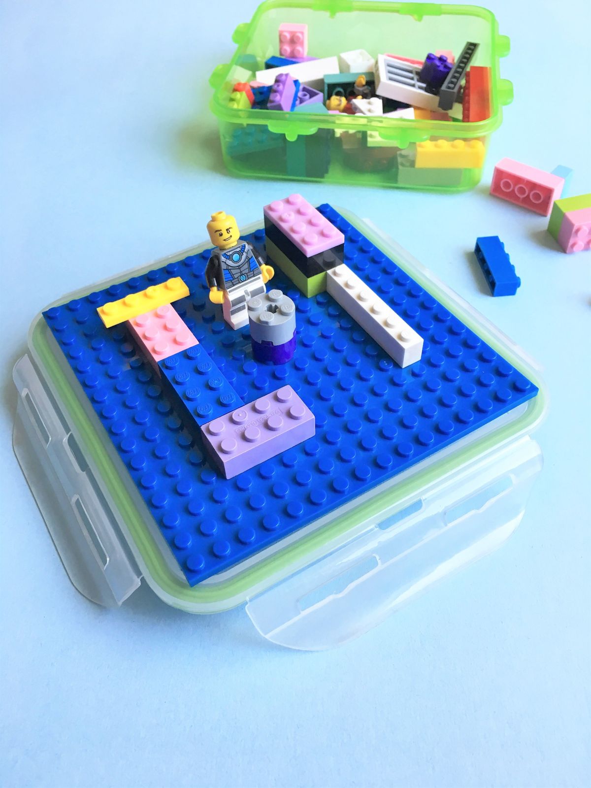 a tupperware container holds mixed lego pieces. in the foreground is the container lid with a lego base and some lego pieces on it
