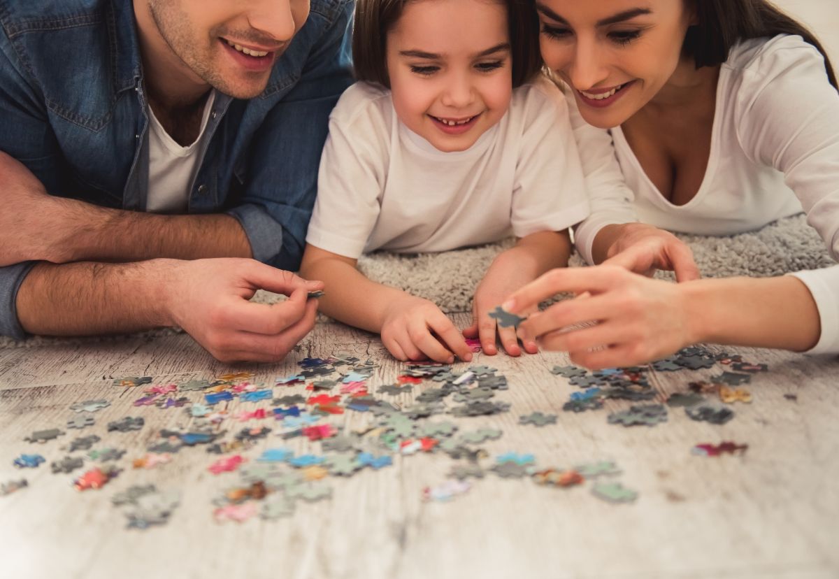 a man, woman and girl sit in front of a pile of jigsaw pieces on a table