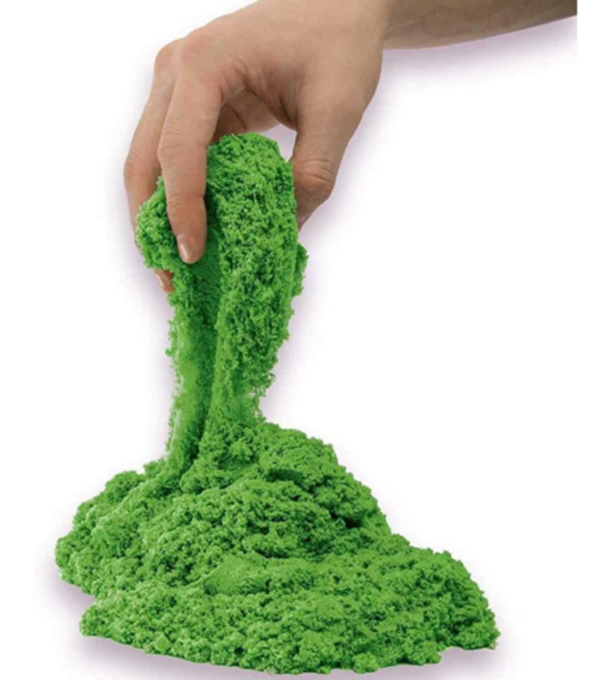 a hand pulls some green kinetic sand out of a pile