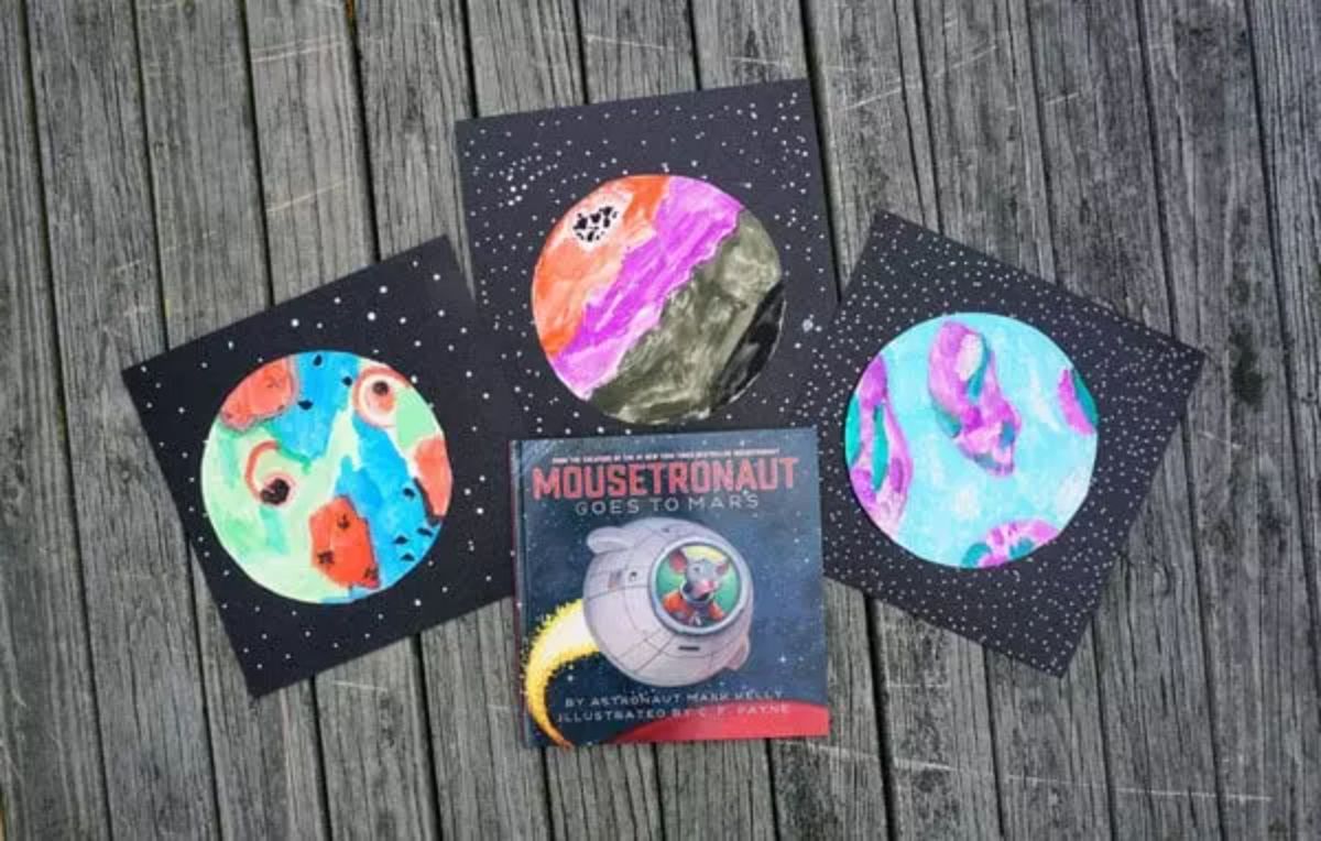 3 black cards with watercolor planets on them. A mousetronaut book is at the front