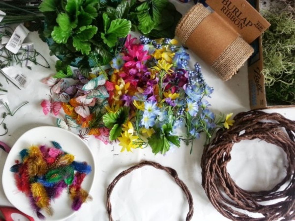 on a table are laid out flowers, wooden woven crowns, feathers, hessian and leaves