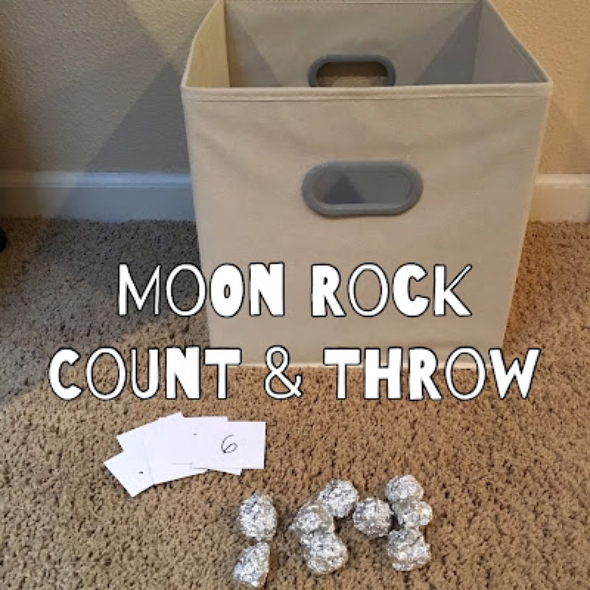 on a camel colored carpet is a begie canvas basket. balls of silver foil are in front of the box with white cards. The text reds "moon rock count and throw"