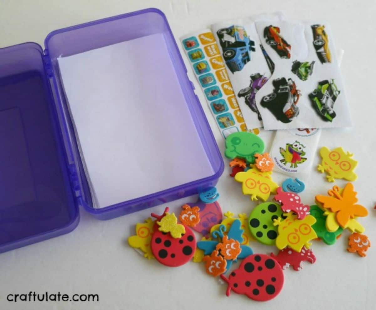 sheets of paper are inside a purple lunchbox, with foam stickers of bugs and sheets of car stickers to the side