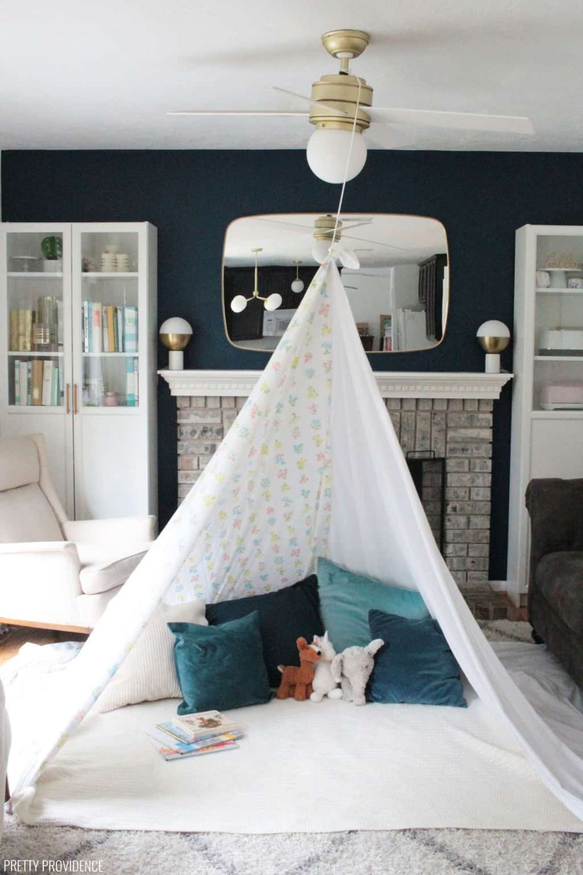 a blanket fort in a living room with cushions, soft toys and books inside