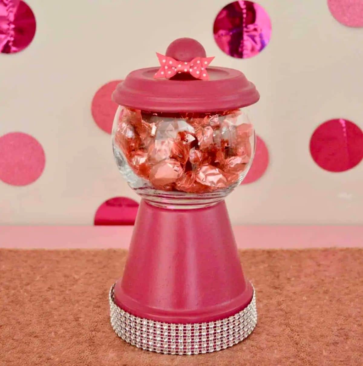 a pink guumball machine filled with wrapped sweets sits on a pink table