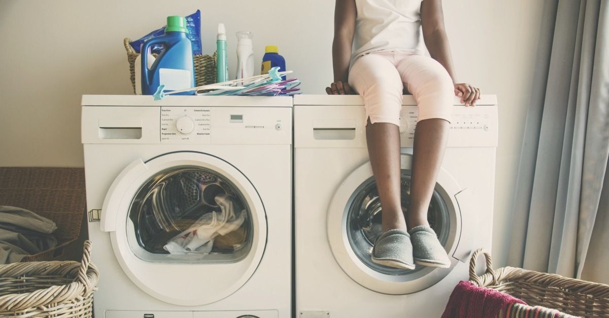 a black child sits on top of a washing machine next to a dryer.