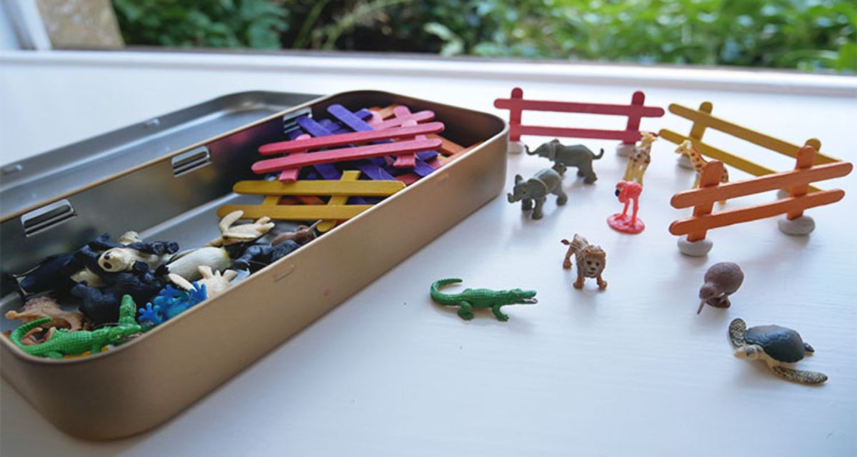 a tin holds plastic toy animals and fencing. To the side is a partially created zoo