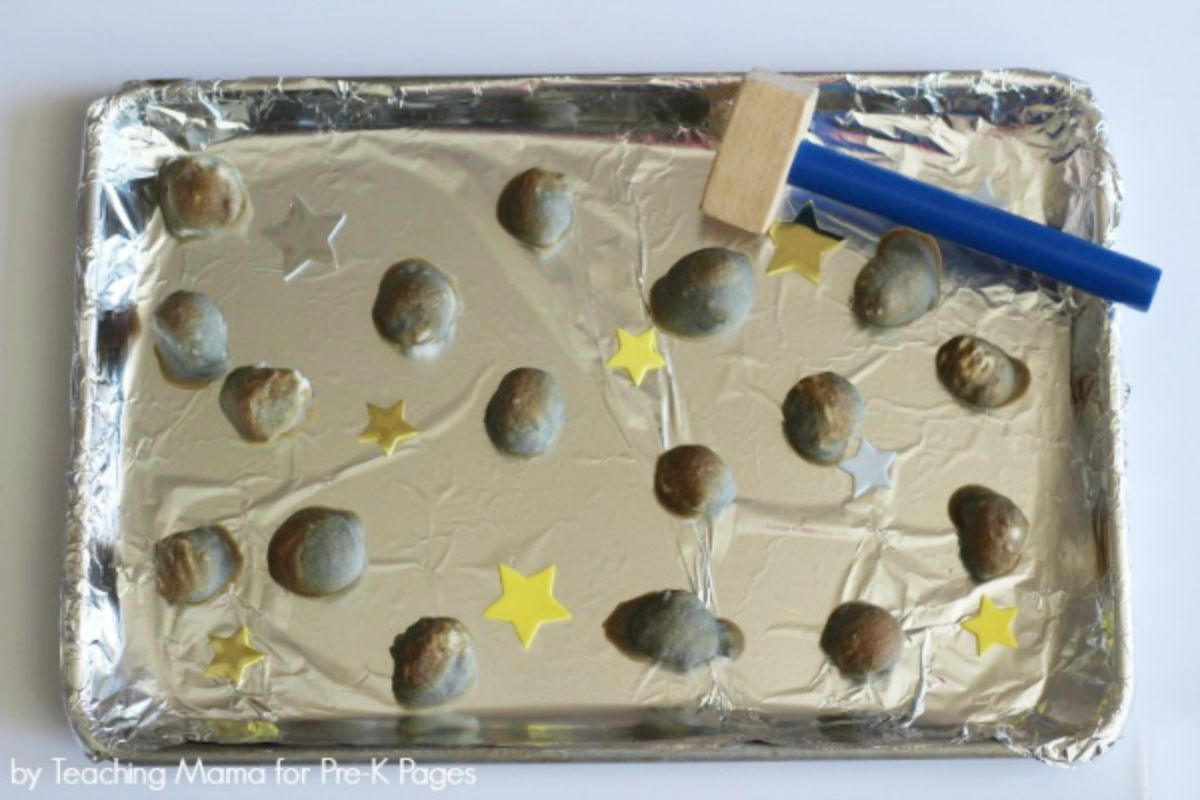 a tray is covered in silver foil with rock shapes scattered on it interspersed with yellow stars. A wooden hammer sits on one side