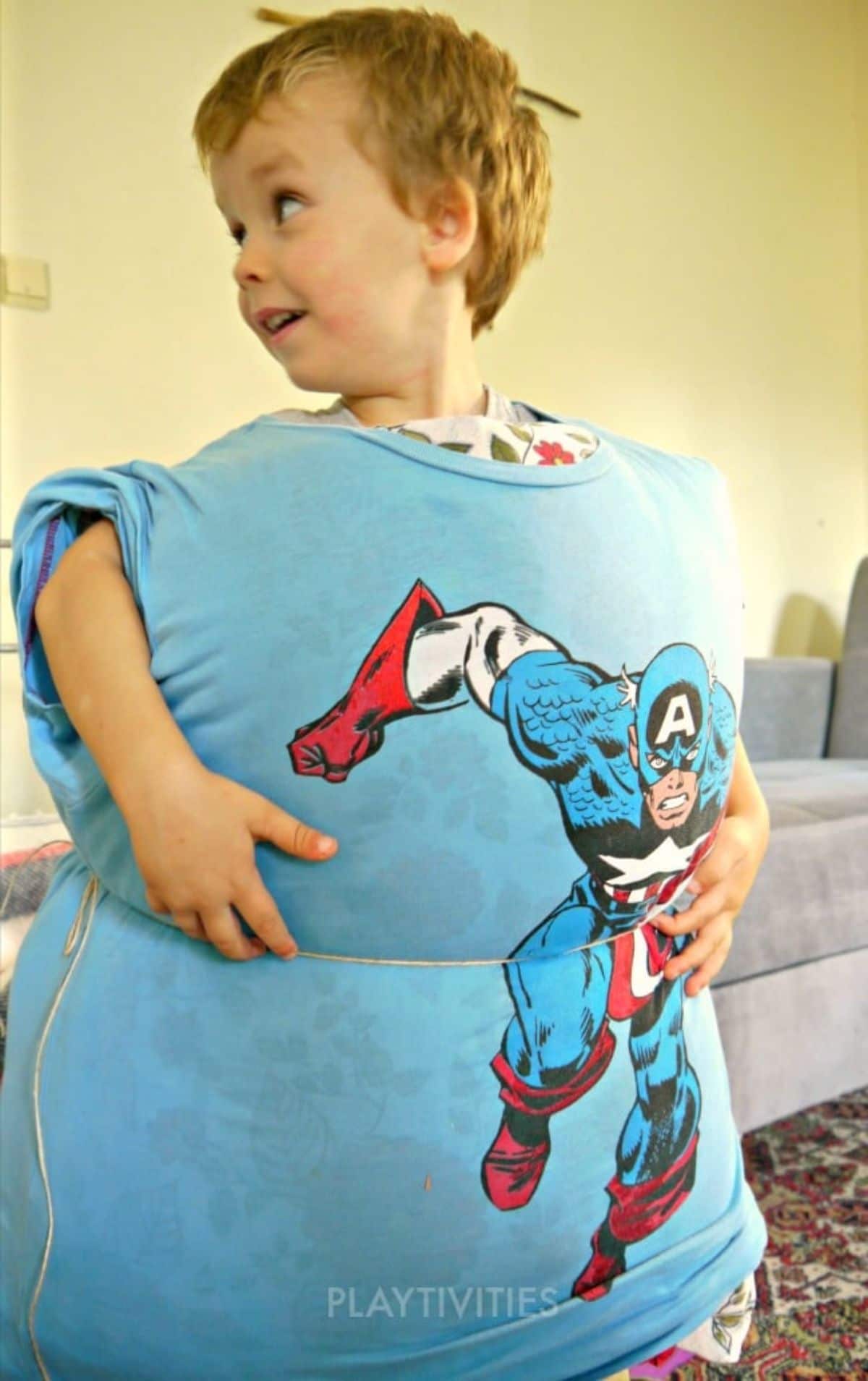 a boy looks ot the left of the screen. He is wearing a blue captain america shirt stuffed with pillows