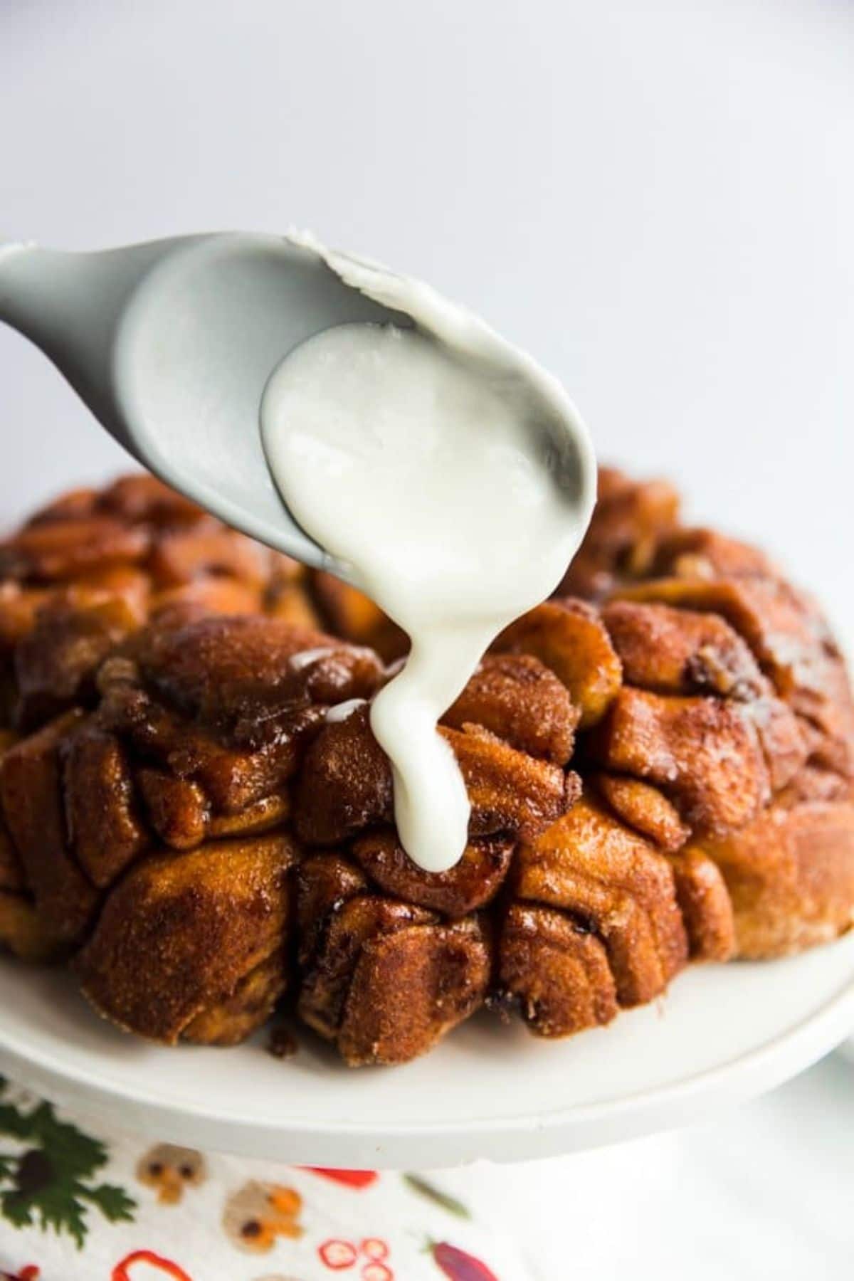 a plate holds a loaf of monkey bread. Frsoting is being dripped onto the top