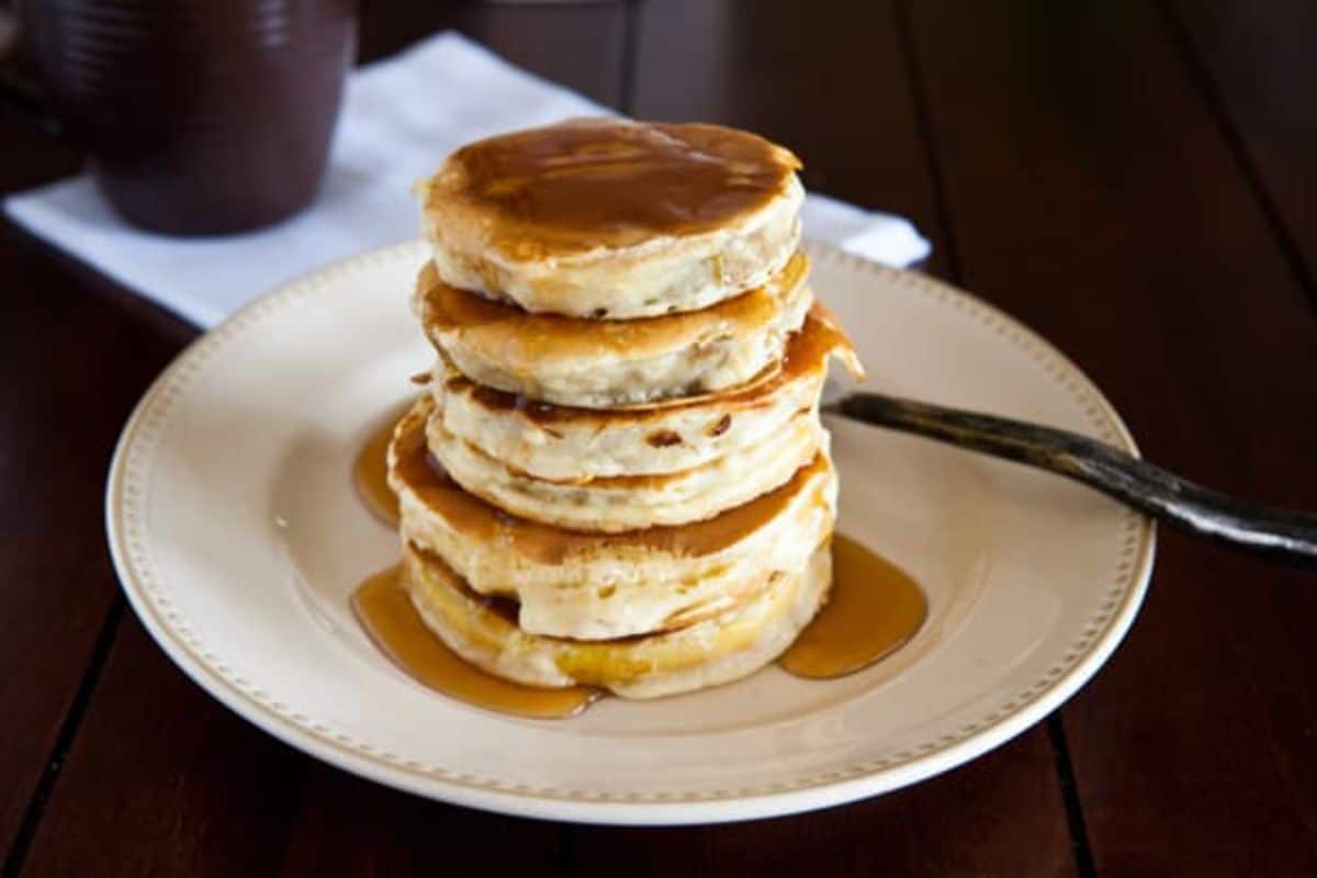 a plate holds a stack of pancakes drenched in syrup