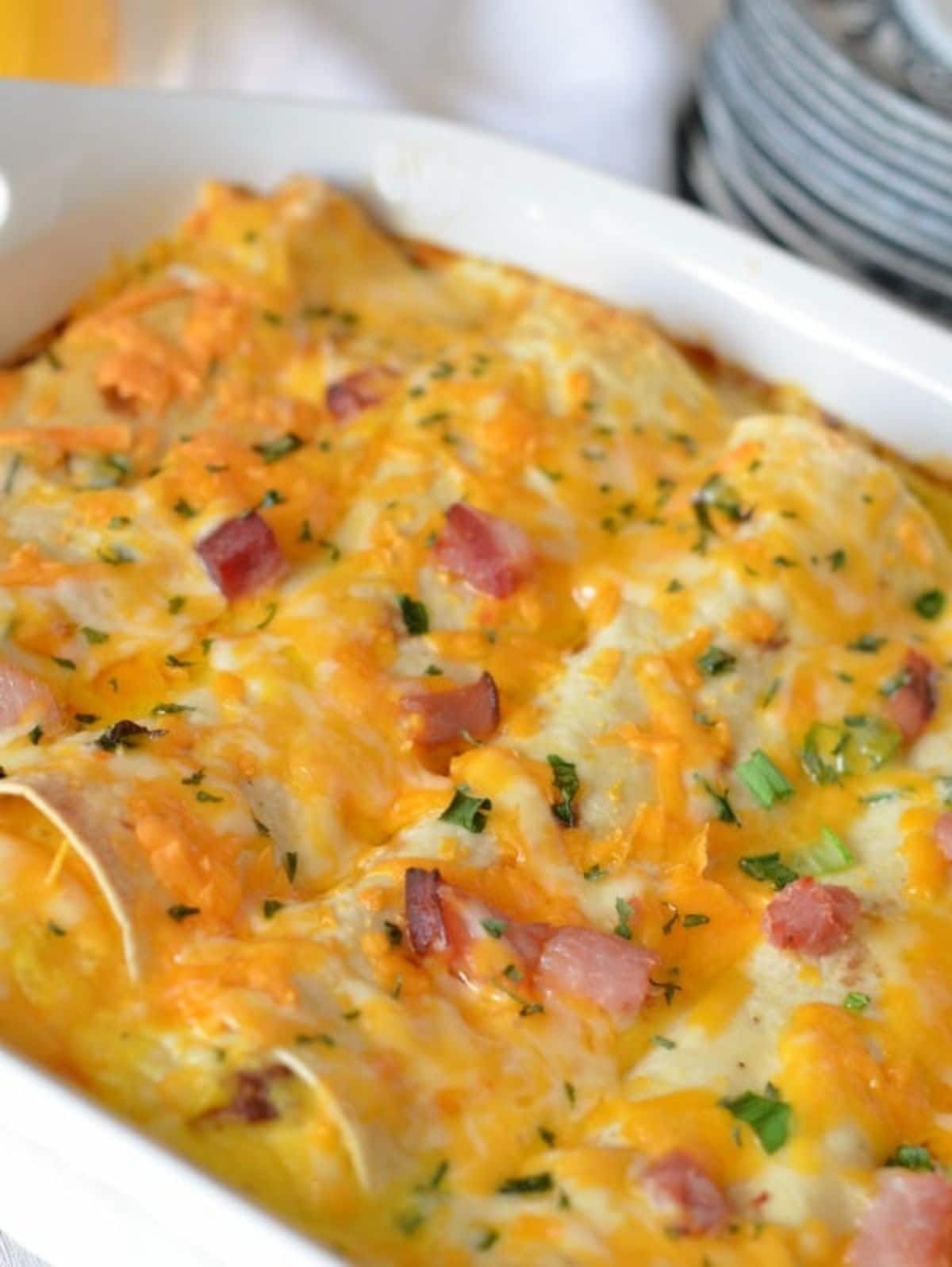 a partial shot of a casserole dish filled with enchiladas, topped with scallions and ham