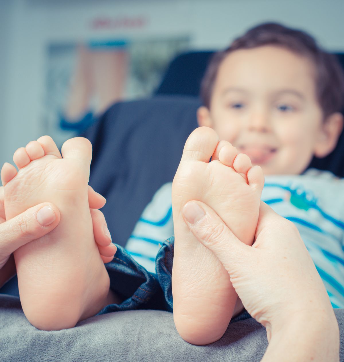 A young boy lays back on a bed while his feet are massaged by adult hands