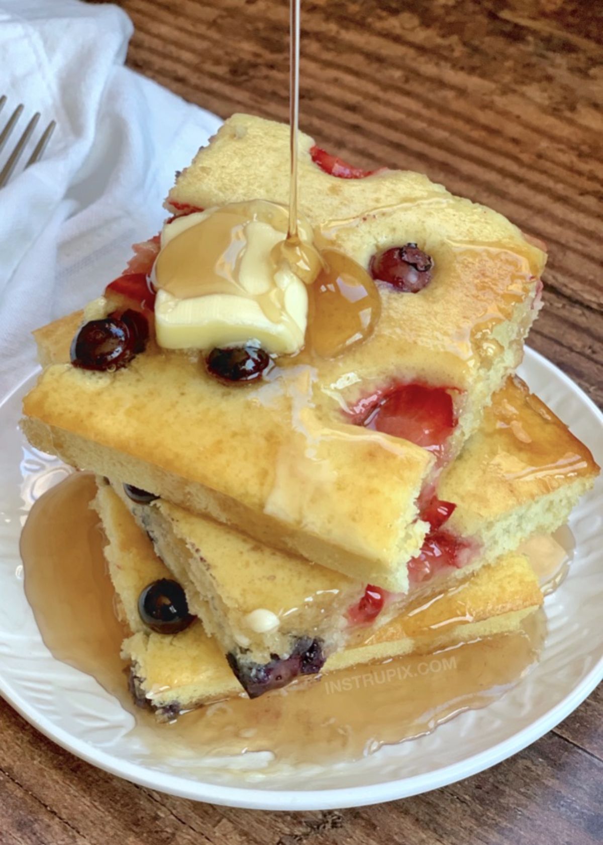 A stack of square pancakes filled with blueberries with syrup dripping over them