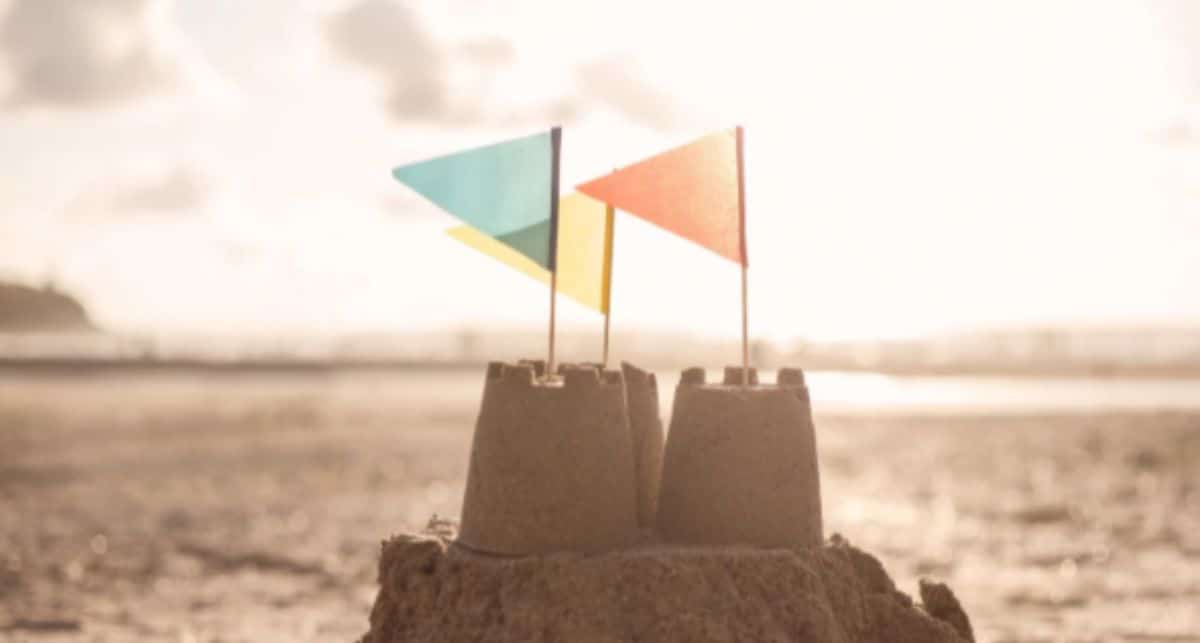 a close up of a sandcastle on the beach with 3 colored flags sticking out of the top