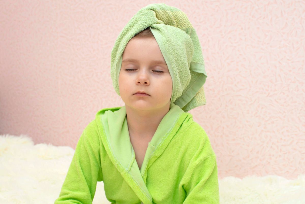 a boy in a green dressing gown and his hair wrapped in a towel has his eyes closed facing the camera