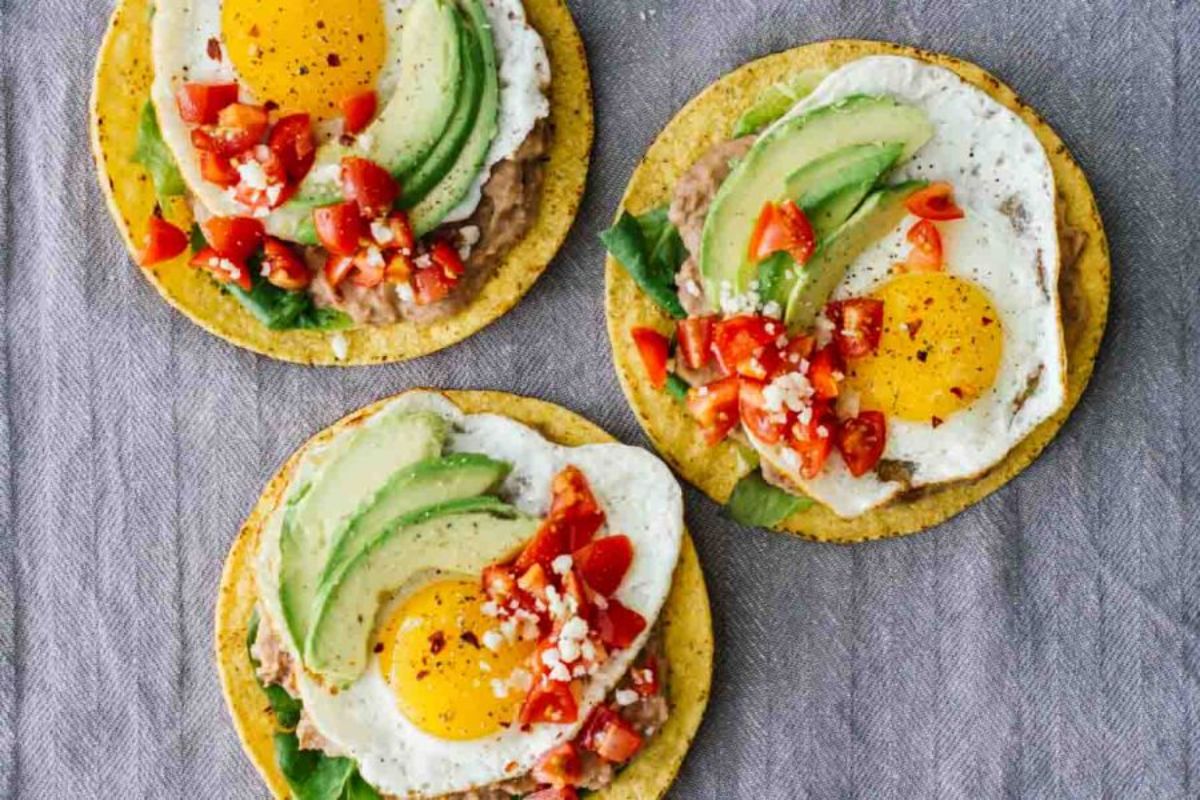3 tortillas topped with spinach, fried egg, avocado slices, chopped tomatoes and feta