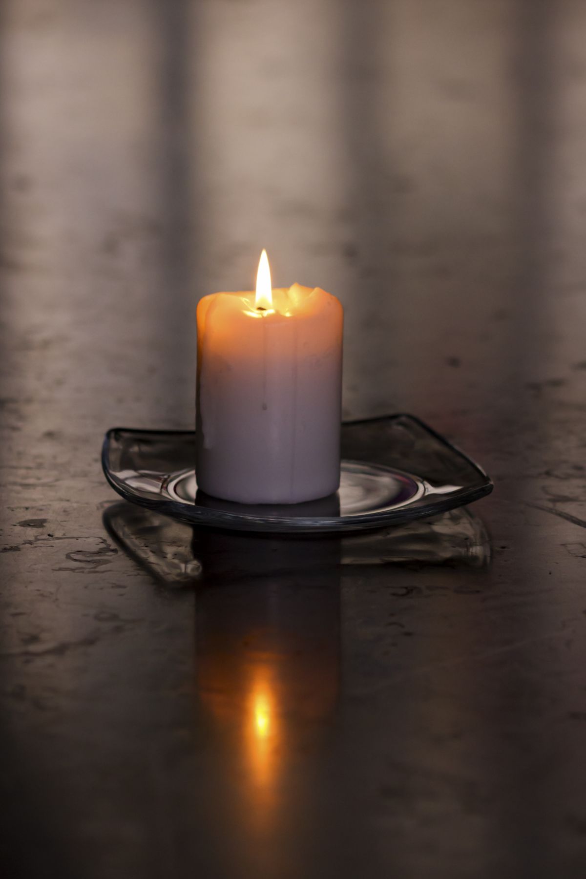 a single lit candle on a glass saucer sits on a table