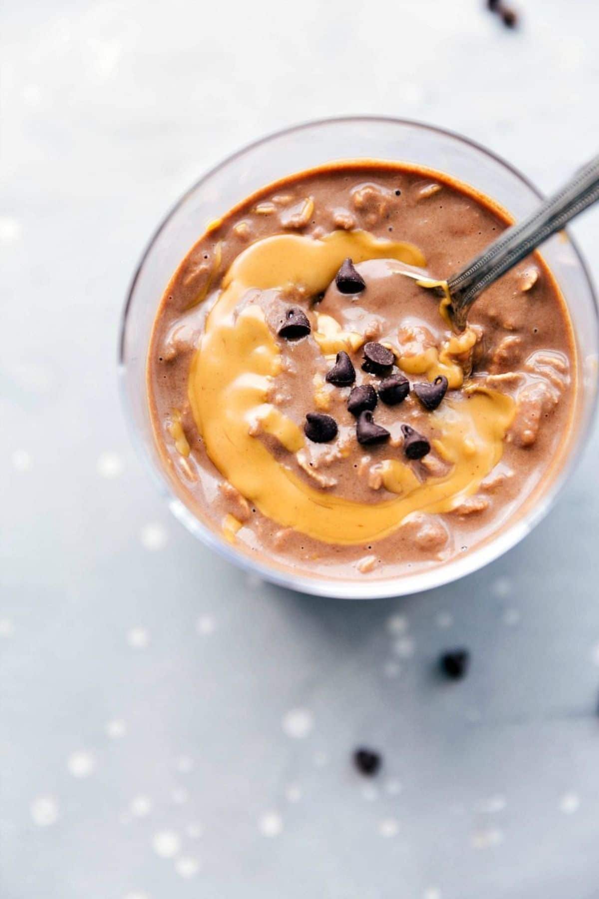 a glass is filled with peanut butter oats, topped with chocolate chips and a spoon sticking out of it