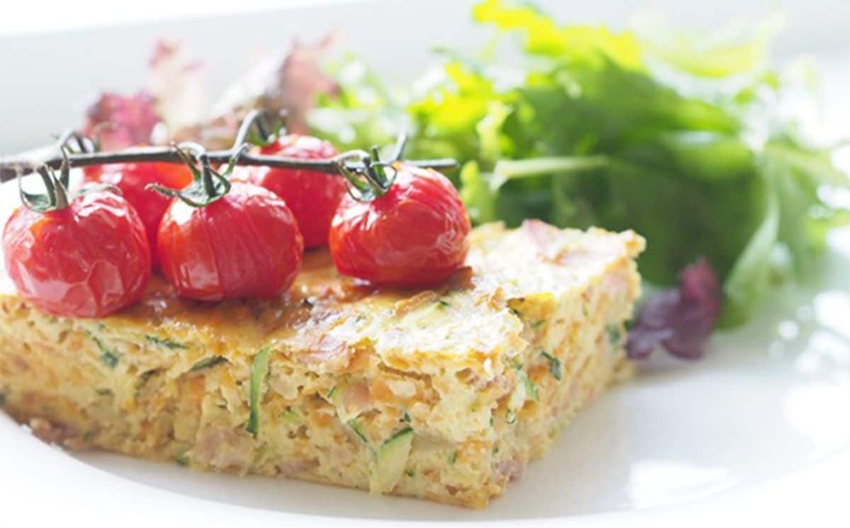 Zucchini and potato slice with cherry tomatoes on a white plate.