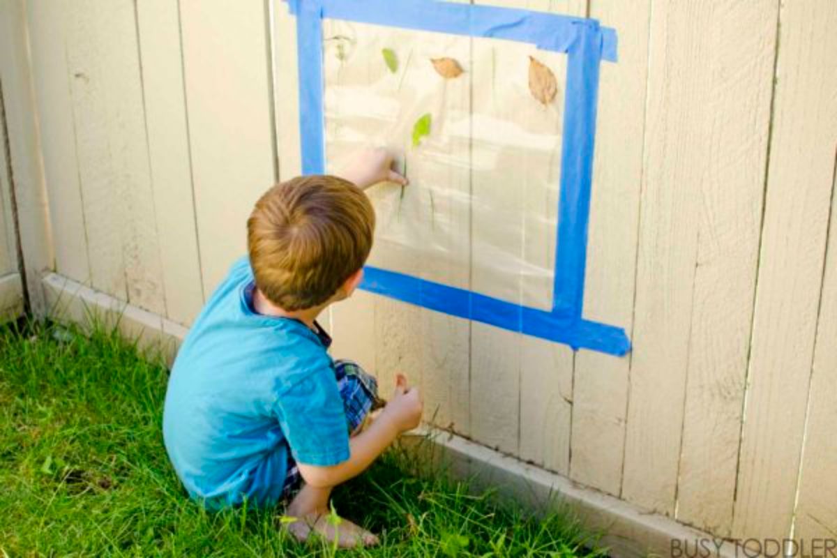 Young boy sticking leaves on a wooden fence