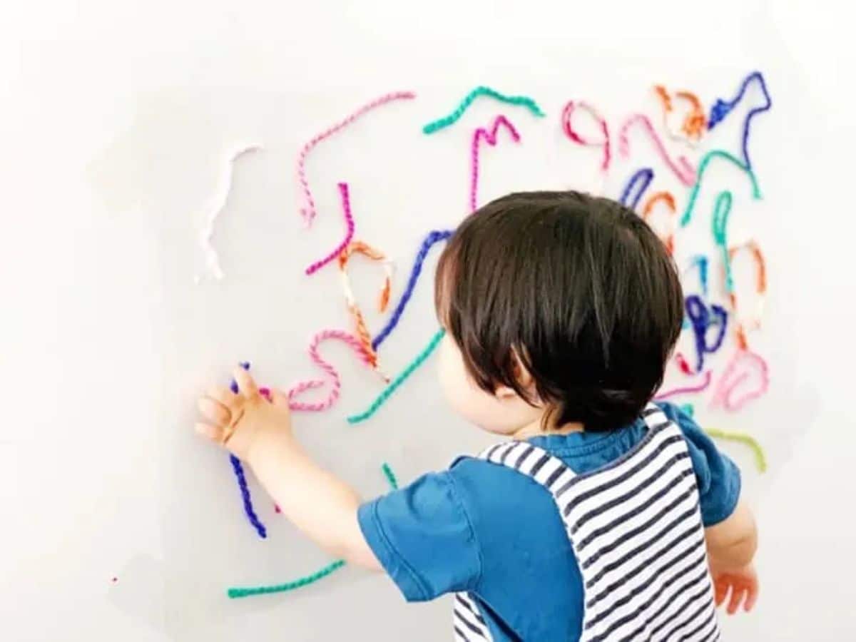 Young kid sticking pieces of colorful yarns on a wall.