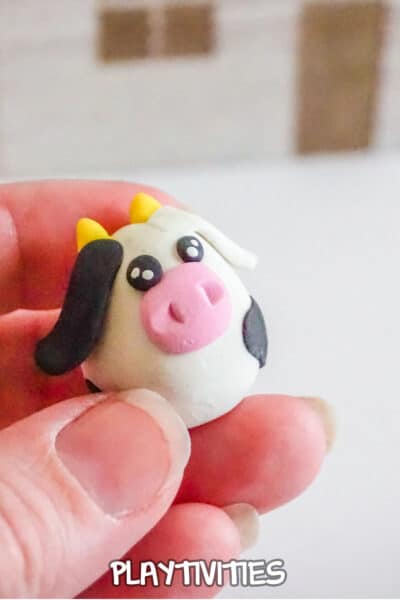 hand holding a tiny cow charm from polymer clay